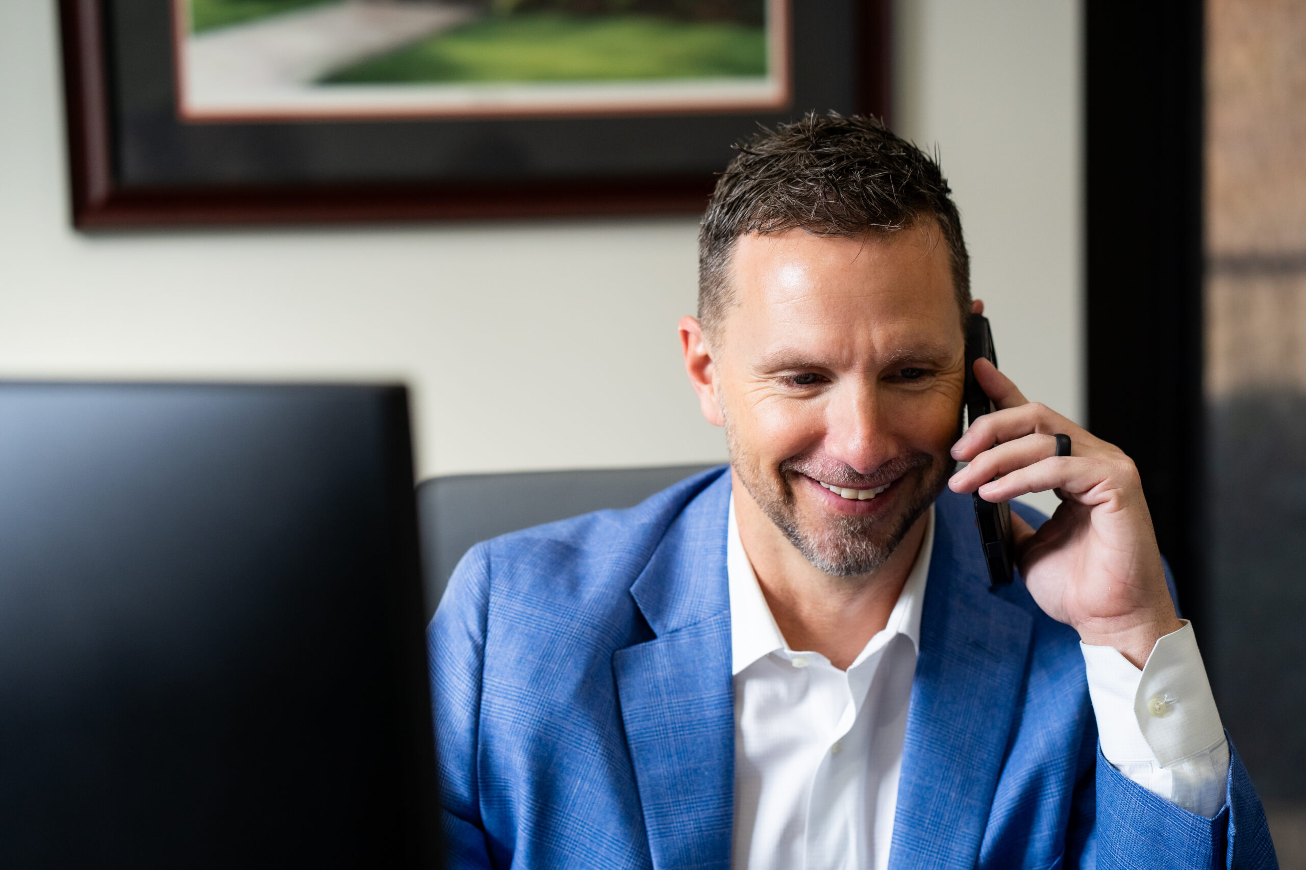 Financial Advisor wearing a blue blazer, taking a phone call with a client in office setting.